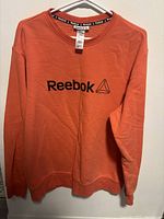 Front view of orange Reebok sweatshirt showing logo and overall condition.