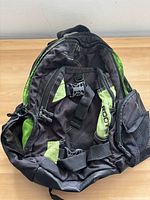 Front view of the Roots hiking backpack showing various pockets, straps, and green accents.