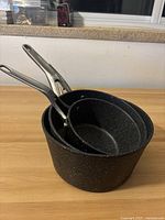 Top view of three nested black granite-effect sauce pans with metal handles on a wooden surface.