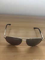 Front view of aviator sunglasses with metal frame and black lenses on wooden surface.