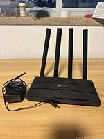 TP Link Archer C80 router powered by a connected power adapter with cable, displayed on a wooden surface.