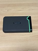 Top view of the black Transcend StoreJet external hard drive with green rubber trim on the corner and Transcend badge in the center.