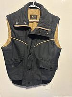 Front view of vintage Sears men's vest showing black exterior, tan lining, collar, snap buttons, and front pockets.