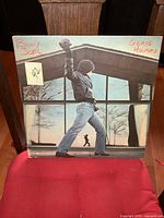 Front cover of the vinyl LP album showing Billy Joel raising a fist in front of a glass house.