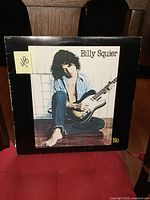 Front cover of the Billy Squier 'Don't Say No' vinyl LP, showing the artist sitting barefoot with a guitar.