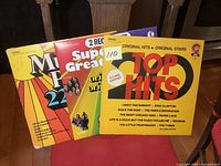 Three vintage hits LP albums displayed together on a wooden chair, showing front covers with colorful artwork.