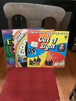 Three vintage hits LP albums arranged upright on a chair, showing colorful album covers with titles partially readable.