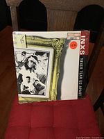 Front cover of INXS Never Tear Us Apart vinyl LP album showing band photo inside yellow ornate frame and price stickers