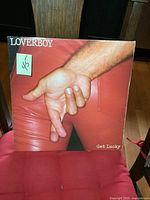 Front cover of Loverboy Get Lucky vinyl album showing a hand over a red background with minor wear and a sticker with pricing