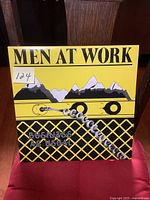 Front cover of the Men At Work 'Business As Usual' vinyl LP album with yellow, black, and white mountain graphics and band name.