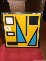 Front cover of Split Enz True Colours LP displaying unique abstract geometric design in yellow, black, white, and blue with band name and album title.