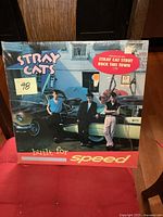 Front cover of the Stray Cats Built for Speed vinyl LP showing the band standing by vintage cars in a city scene with a sticker highlighting songs.