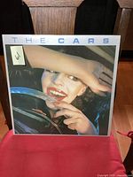 Front cover of The Cars self-titled vinyl LP featuring close-up photo of a woman holding a car steering wheel and smiling.
