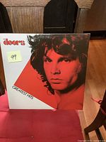 Front cover of the album showing red and white design with Jim Morrison's red-tinted face and text 'The Doors Greatest Hits'
