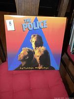 Front cover of The Police "Zenyatta Mondatta" album with three band members' portraits on a blue triangular background set against an orange gradient.