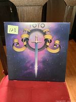 Front cover of Toto vintage vinyl LP album featuring a sword emblem against a cosmic purple background.