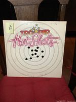 Front cover of Trooper Hot Shots vinyl LP album showing bullet hole target design and title text.