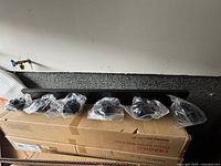 New black metal 6-light vanity light fixture laid out on top of unopened box. Each glass shade individually wrapped in plastic for protection.