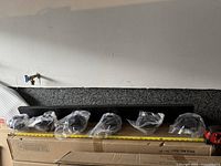 Black metal track light bar with six lights in plastic protective packaging laid out along the bar across a surface.