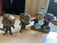 Three Marvel Funko Pop bobbleheads on table with a water bottle in background, showing two Thanos and one Thor figure