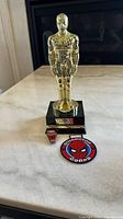 Gold-colored Spider-Man trophy on black base with Marvel Collector Corps enamel pin and patch shown together