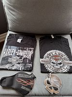 Two black Harley Davidson men's t-shirts, one with 'Harley-Davidson Genuine' design and one Orlando Florida skull design; Harley Davidson face mask with flame graphics; metallic silver leather skull-shaped coin purse.