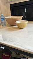 Two vintage glazed stoneware mixing bowls on a table next to a water bottle for scale, one large approx. 11 inch bowl and a smaller bowl
