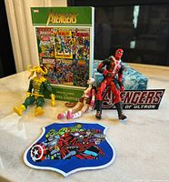 Photo showing Loki, Gwenpool, and Deadpool figures, one large Avengers jacket patch, hub snap, and Official Index to Marvel Universe book