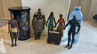 Photo of 7 Black Panther figurines and a themed cup on a flat surface, next to a water bottle for scale