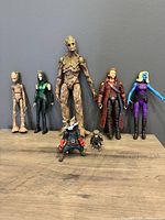 Front view of 7 Marvel Legends Guardians of the Galaxy figures arranged side by side including Groot (large and teenage), Rocket Raccoon (regular and LEGO mini figure), Star-Lord, Mantis, and Nebula.