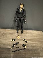 Front view of Black Widow figure standing with accessories laid out before it including alternate head, hands, pistol, baton, and cylindrical piece.