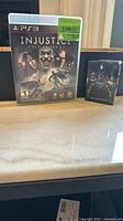 Front of PS3 game case for Injustice: Gods Among Us and sealed Injustice 2 playing cards box
