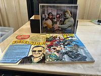 Photo showing 2019 Comic-Con souvenir book with Marvel superhero characters on the cover accompanied by a laminated Stan Lee Excelsior note and a clear case with the photograph of Stan Lee with Lou Ferrigno and another costumed character.