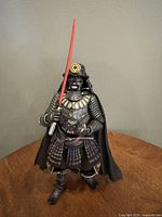 Front view of Darth Vader samurai figure holding a red lightsaber, standing on a wooden surface with neutral background.