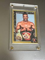Front of the card showing Evander Holyfield with championship belts, gold border, in screw down acrylic case