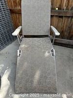 Full view of the outdoor reclining chaise lounge chair showing beige patterned fabric upholstery, padded backrest and seat, adjustable backrest, fold-out leg rest, and molded plastic armrests.