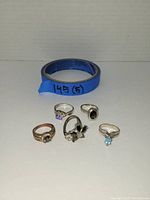 Five assorted fashion rings arranged with blue tape roll in background