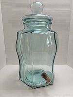 Photo of vintage green glass beverage dispenser with brass spigot and glass lid, showing rounded square body shape and clear lid with knob.