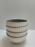 Stacked four ceramic dip bowls showing ribbed creamy white exterior and dark gray interior