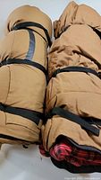 Two rolled up sleeping bags side by side secured with black compression straps, brown exterior.