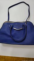 Blue leather handbag showing front with shoulder strap and dual handles.