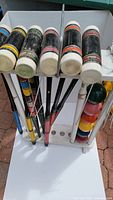 Full view of six wooden mallets with multicolor striped handles and white heads on the white wooden storage stand. Some paint chipping is visible on mallets.