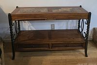 Full view of console table showing wooden top with stone inlays, metal frame with scrollwork and twisted leg accents, two drawers and lower wooden shelf