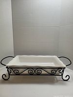 White rectangular stoneware dish set in black metal rack with decorative scrollwork and handles, front angle.