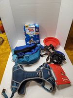 Photo of blue and black Kurgo dog harnesses, red collapsible bowl, blue waist pouch, and pack of Wee-Wee training pads