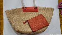 Straw tote bag with red leather accents and matching red pouch on white background.