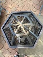 Top view showing hexagonal shape of metal fire pit with mesh cover and included fire poker resting across the top.