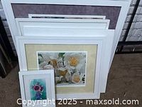 Five floral art prints stacked together. The largest print shows white flowers with yellow centers. A smaller print with vibrant flowers on a teal background is visible in front.