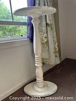 Photo of white distressed wood pedestal plant stand with turned detailing near window and floral curtains