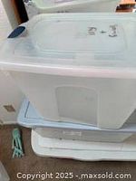 Close-up of large clear plastic storage bin with locking lid, showing general condition and size relative to bins below.